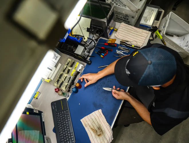Person working on a knife repair task at a desk with tools and components.