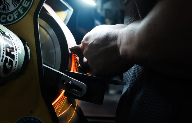 Person using a sharpening a blade on a belt grinder with sparks flying
